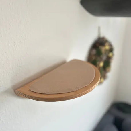 Halbkreisförmiges Wandregal aus Holz mit hellbraunem Kissen.