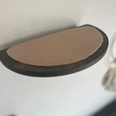 Halbkreisförmiges Wandregal mit hellbraunem Kissen.