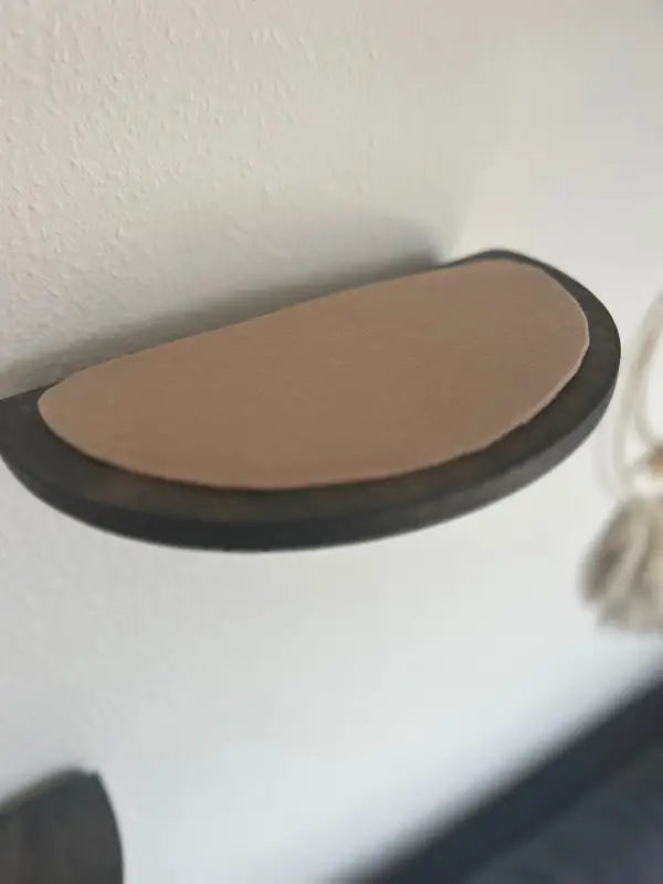 Halbkreisförmiges Wandregal mit hellbraunem Kissen.